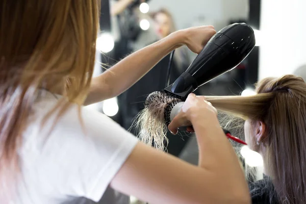 Drying long blonde hair with hair dryer and round brush.