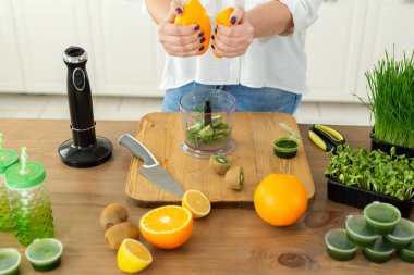 Buğday suyu kokteyli yapmak için portakal suyu sıkan bir kadının yakın çekimi. Beyazotlar, sağlıklı yiyecekler.