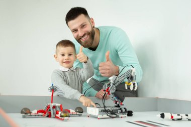 Mutlu yakışıklı adam, lego robotlarla oynarken neşeli küçük oğluyla kameraya gülümsüyor ve baş parmağını gösteriyor..