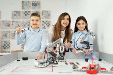 Genç ve güzel bir anne, oğlu ve kızıyla birlikte robotlarla birlikte robot okulunda poz veriyor..
