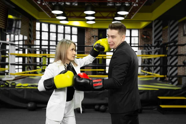 Businessman and a businesswoman sparring with boxing gloves against of a boxing ring.