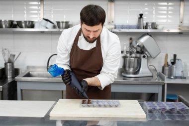 Çikolatacı çikolatayı kalıplara döküyor. Pasta poşeti şefi erimiş çikolatayı silikon kalıba dolduruyor..