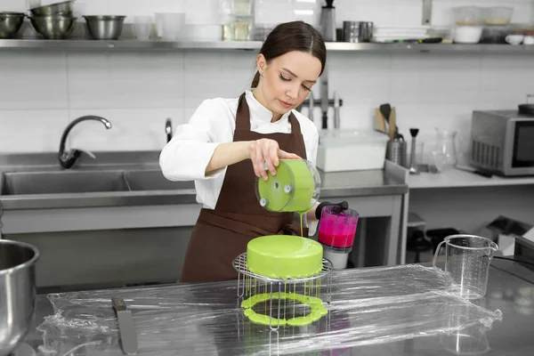 Female pastry chef decorates a mousse cake with a mirror glaze.