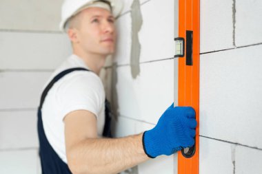 Beyaz başlıklı güzel bir mimar ya da inşaatçı düz bir araçla duvarın seviyesini kontrol eder