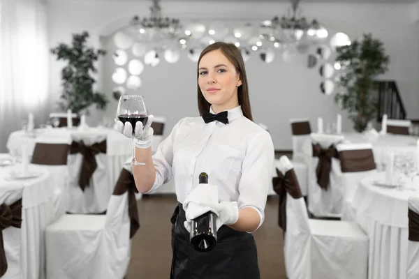 戴白色手套的女服务员拿着杯子和一瓶红酒 — 图库照片