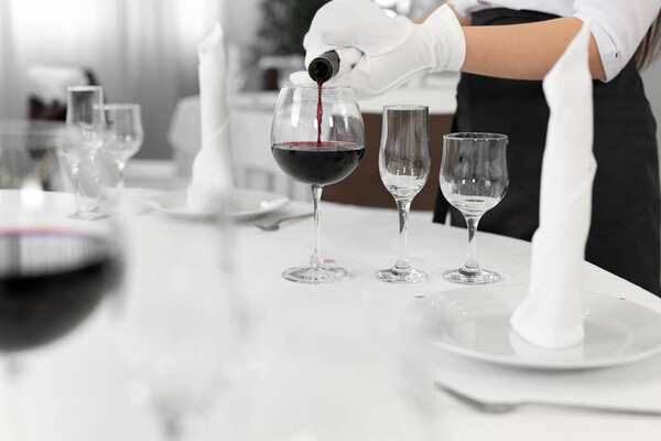 Close-up of a waiters hand pouring red wine into a glass