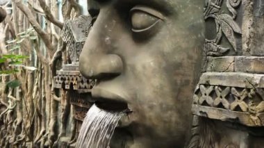 Ormandaki bir tanrının ağzında şelale olan eski bir taş heykeli.