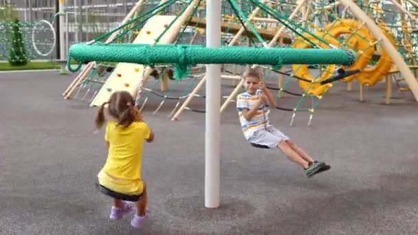 男の子と女の子 現代の遊び場で遊ぶ カルーセルに乗る — ストック動画