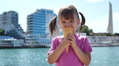Neşeli küçük kız deniz kıyısında dondurma yiyor.