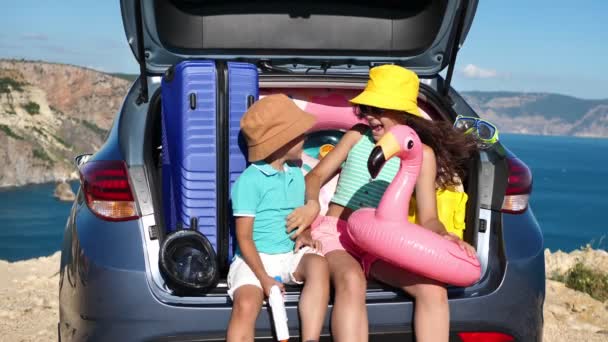 子供たちはスーツケース付きの車の近くで楽しみを持っています 海によって膨脹可能な円 — ストック動画