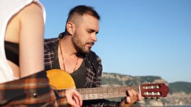 Denize bakan bir dağın tepesinde aşık bir çift. Adam gitar çalar, kadın şarkı söyler.