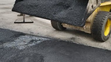 Traktörün kovasından yeni, sıcak asfalt dökülüyor. Yol onarımları