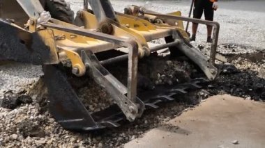 Kazı makinesinin kovası eski asfaltı kırıyor. Yolun sökülmesi ve onarımı üzerinde çalış.