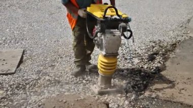 Bir işçi yol tamiri sırasında taşınabilir titreşim tamponu kullanır.