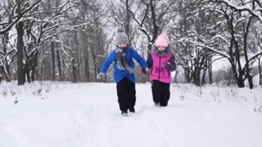 Çocuklar, bir oğlan ve bir kız el ele tutuşup kışın ormanda koşarlar.