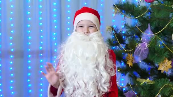 クリスマスツリーの近くのサンタクロースの衣装の男の子は彼の手を振る — ストック動画