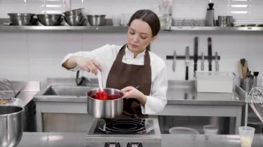 Kadın pasta şefi, profesyonel bir mutfakta pastayı doldurmak için tencerede böğürtlen konservesi hazırlıyor..