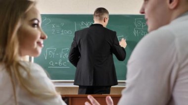 Öğrenciler konuşur ve derse müdahale ederler. Öğretmen tahtaya formüller yazar..