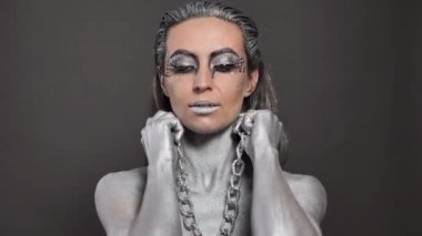 Güzel bir kadın, cildinde gümüş boya, saçlarında da zincir var..