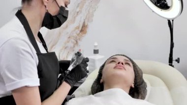 Kaş mikropatinajı kavramı. Güzellik uzmanı kalıcı makyaj için dövme makinesine boya yazıyor..