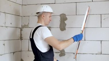 Beyaz başlıklı güzel bir mimar ya da inşaatçı düz bir araçla duvarın seviyesini kontrol eder.