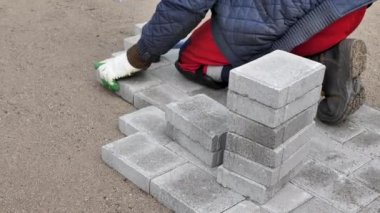 Kauçuk çekiçle beton bloklar döşeyen bir işçinin elleri.