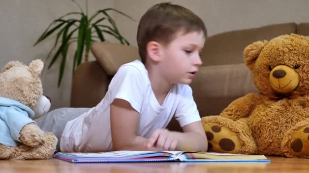 Niño Feliz Está Leyendo Libro Juguetes Esponjosos Tumbado Piso Cálido — Vídeos de Stock
