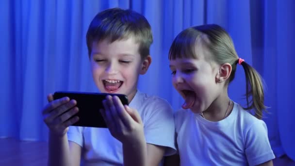 暗闇の中で携帯電話のカメラで楽しそうに笑っている子供たち 兄弟姉妹 — ストック動画