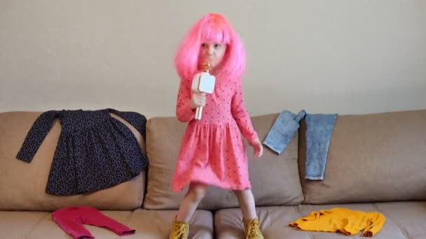 Mała Dziewczynka Różowej Peruce Śpiewa Mikrofonu Skacze Kanapie Wśród Rozrzuconych — Wideo stockowe