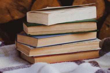 Eski tarz ahşap arka planda yün battaniyenin üzerinde eski kitaplardan oluşan bir yığın. Edebiyat, eğitim, hobi, okuma ve yaşam tarzı