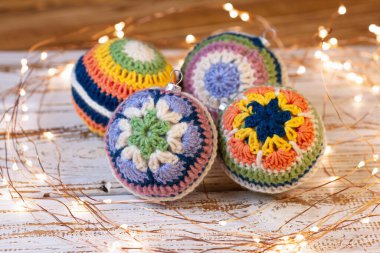 Noel ağacı için tığ işi süslemeler. Farklı renkli dantelli, parlak toplar. Beyaz ahşap arka plan ve yol gösteren ışıklar