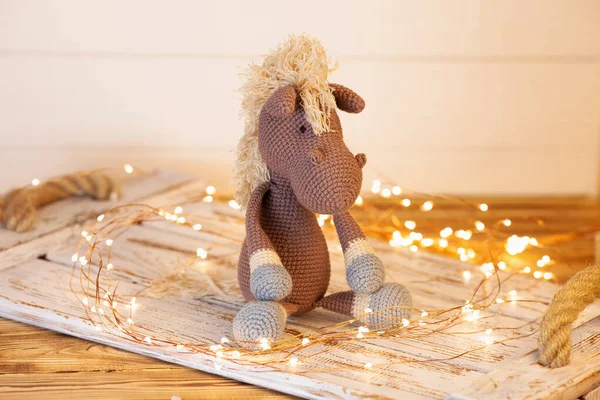 a wonderful crocheted soft toy. A figure of a brown horse with a beige mane. On a wooden background behind bright led lights