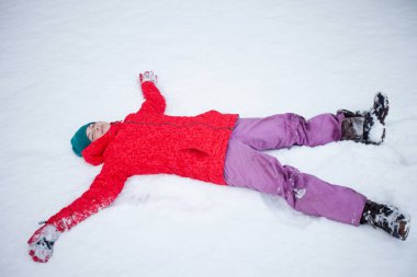 Genç bir kız taze karda yatar ve bir kar meleği yapar. Dışarıda kış eğlencesi, karlı bir parkta aile zamanı.