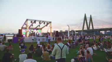 KAZAN, TATARSTAN RUSSIA - 27 Haziran 2021: İnsanlar şehir parkındaki yeşil çayır çimlerinde gün batımında yavaş çekimde oturmaktan zevk alırlar. 27 Haziran 'da Kazan' da vatandaşlar için tatil etkinliği