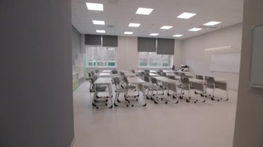 Boş sınıfta beyaz tahtanın karşısında sandalyeli öğrenci masaları. Yenilenmiş okulda çağdaş ekipmanlar