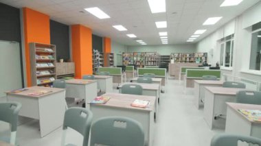 Okulda küçük masaları ve kitaplıkları olan boş bir okuma odası. Farklı edebiyatla aydınlatılmış çocuk kütüphanesi