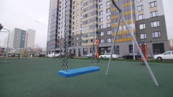 大きなアパートの建物の近くの空の遊び場でチェーン付きの青いスイング 子供ゲーム用機器 — ストック動画