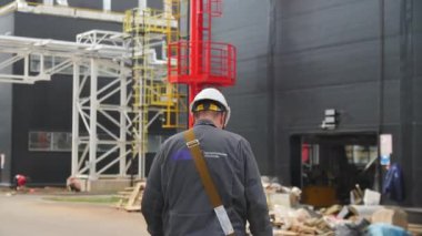 ALMATY, KAZAKHSTAN - 26 Ekim 2022: çapraz-gövde torbası ile işçi bitki bahçesinin arka görünümünde yürür. Çağdaş üretim kompleksi, 26 Ekim 'de Almaty' de