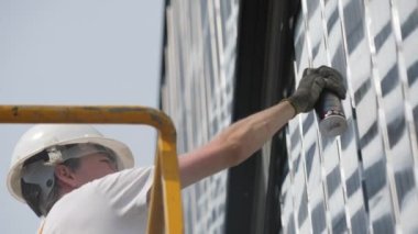 ALMATY, KAZAKHSTAN - 26 Ekim 2022: Eldivenli sanatçı, endüstriyel beşikte beyaz renkte bina cephesi çiziyor. 26 Ekim 'de Almaty' de atölyenin dış yüzeyi için şık bir model.