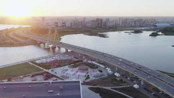 日没の上部ビューで川岸堤防上の交通ミレニアム橋とスポーツグラウンド 都市インフラ整備 — ストック動画