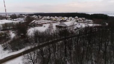 Araba, kış günü hava manzaralı karlı arazide büyük bir hangara gidiyor. Banliyö bölgesinde sanayi deposu.