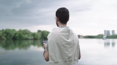 ALMATY, KAZAKHSTAN - 26 Ekim 2022: Tabletli adam sakin nehre bakar ve kasvetli gökyüzü altında kameraya döner. Mühendis 26 Ekim 'de Almaty' de yeni bir proje düşünüyor.