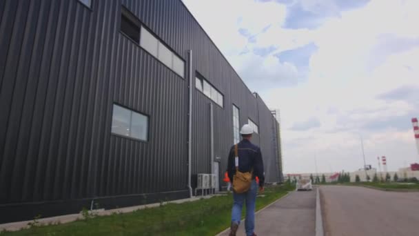 Pracovník Křížovou Taškou Helmou Prochází Kolem Velké Černé Dílny Budovy — Stock video