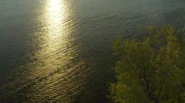 Göldeki göl suyunda gün batımının parlak yolu ve bankanın hava manzaralı parkı. Resimli nehir kenarı yaz akşamı alacakaranlıkta