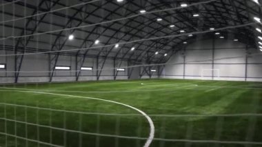 Spor merkezi binasında yemyeşil çim ve koruyucu ağ olan boş bir futbol sahası. Futbol antrenmanı için büyük bir hangar.