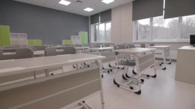 Büyük pencereli boş sınıflardaki öğrenciler ve raflar için masa ve sandalyeler. İlkokul binasının modern iç mimarisi