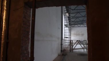 İnşaat alanındaki büyük yenileme odasındaki inşaatçılar için iskeleler. Malzemelerle fabrika yenileme süreci
