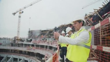 ALMATY, KAZAKHSTAN - SEPTEMBER 07 2022: Ana mühendis, Tribün ağır çekimde takım ile tamamlanmamış spor arena binasının fotoğrafını çekiyor. İnşaat alanı 07 Eylül 'de Almaty' de