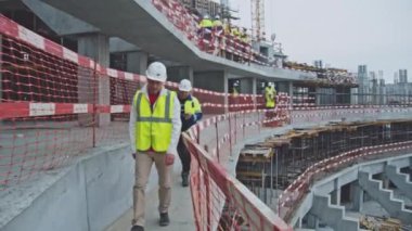 ALMATY, KAZAKHSTAN - Eylül 07 2022: miğferli baş mühendis ve ustabaşı inşaat alanında spor arenası boyunca ağır çekimde yürüyor. Almaty 'de Eylül 07' de bina teftişi