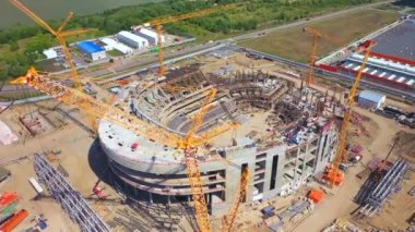 Güneşli şehir hava manzarasında inşaat alanında renkli vinçleri olan büyük bir spor stadyumu. Kentsel gelişim süreci